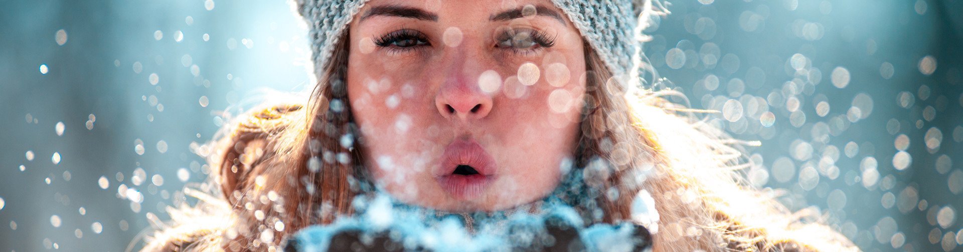 [Translate to Deutsch (Schweiz):] Frau mit Mütze pustet Schnee in die Kamera